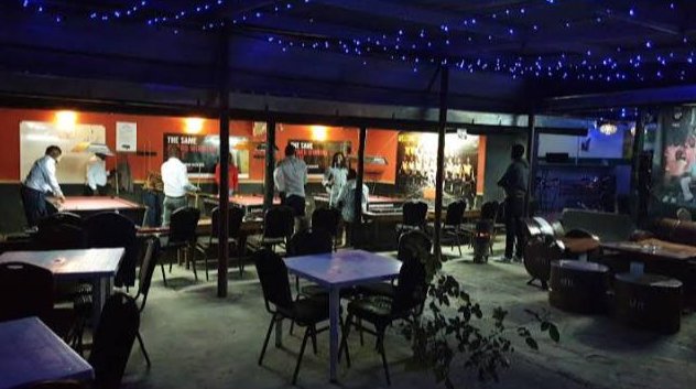 The Spice Pool Club floor at night: pool tables under orange walls, an open-air seating area with string lights overhead